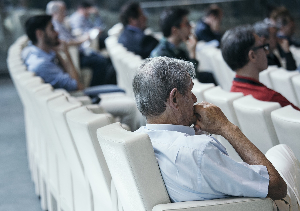 Older person sitting in an auditorium with a younger audience in the background