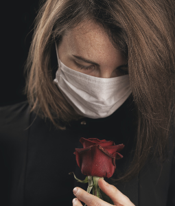 Person with mask looking at a rose